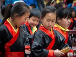 Children wearing traditional robes are learning Chinese calligraphy using water brushes.